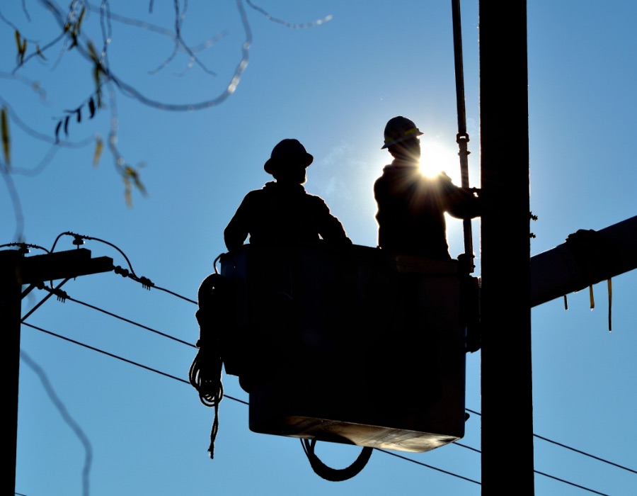 Silhouette of two lineman in a bucket doing repairs